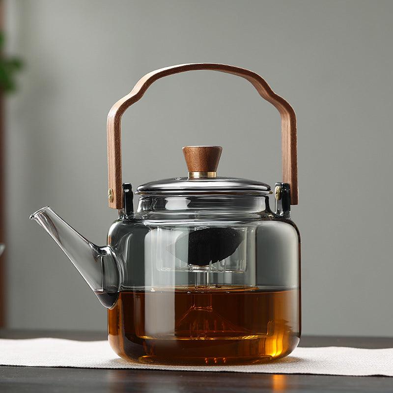 Smoke glass teapot with wooden handle filled with tea and infuser on a table