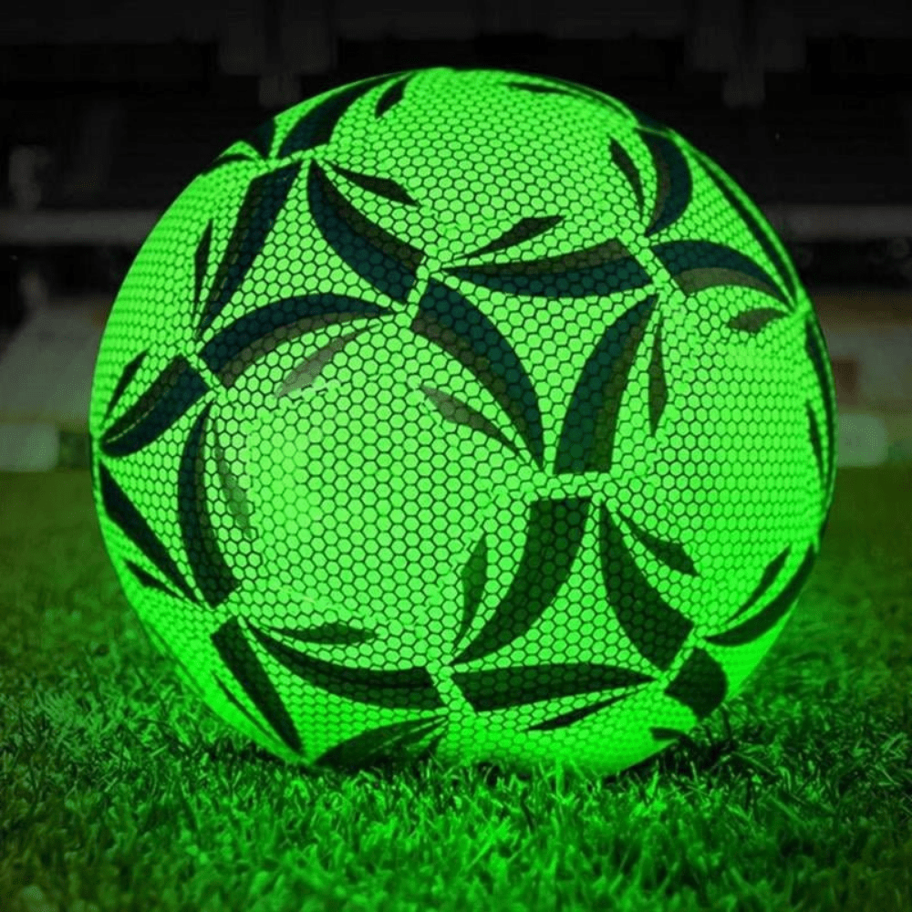 Glow-in-the-dark soccer ball illuminated in green on a grass field at night