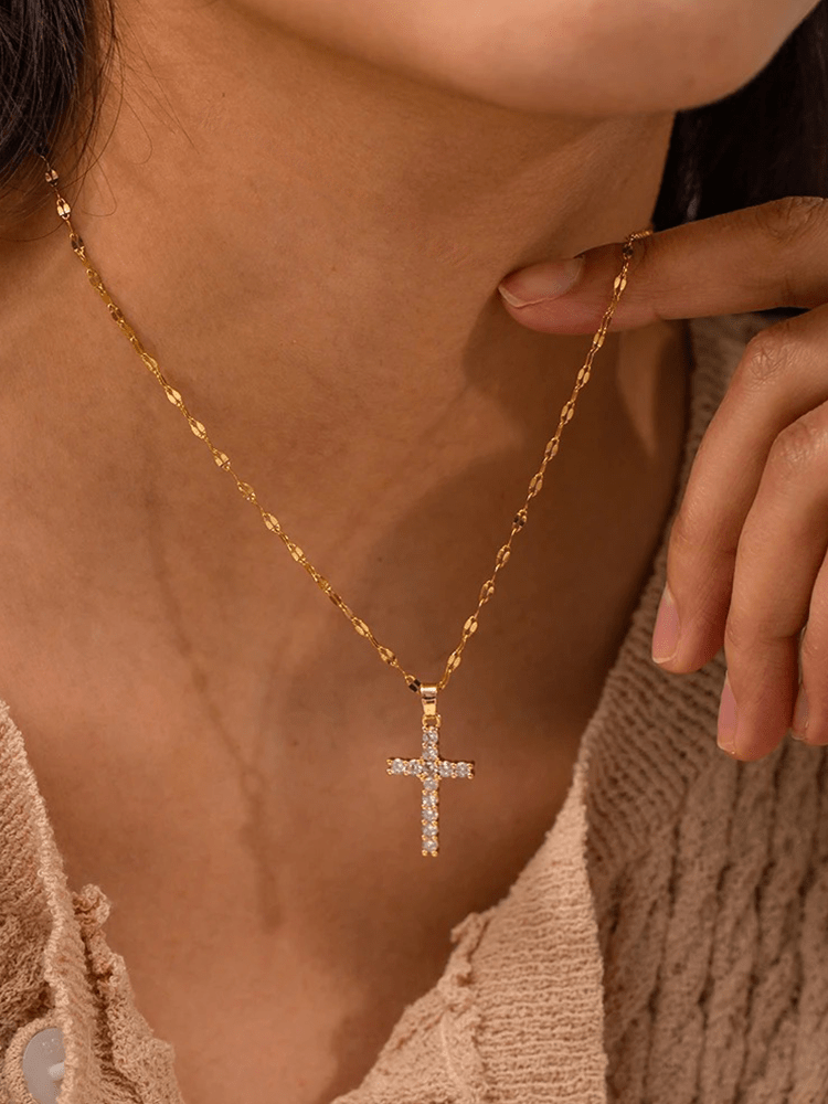 Close-up of a woman wearing a gold-plated cross pendant necklace with sparkling crystals.