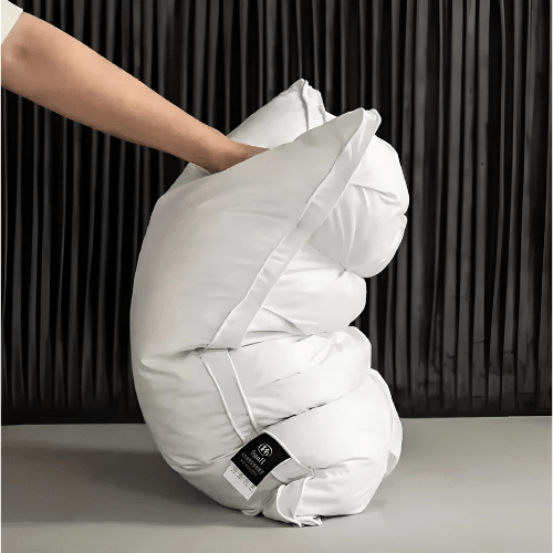 A hand compressing a soft white pillow to demonstrate flexibility and plush filling