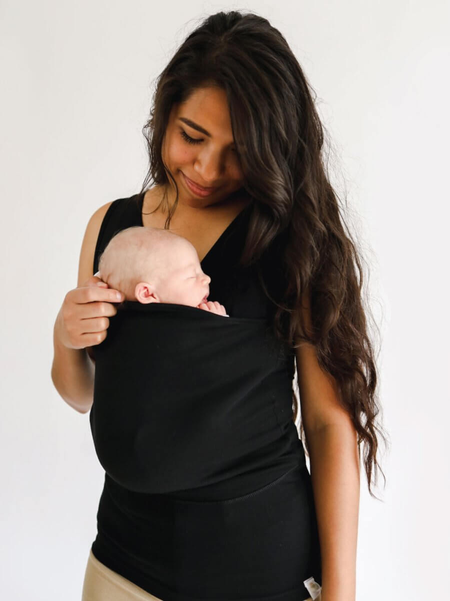 Mother wearing a black handsfree wrap baby carrier with a sleeping infant