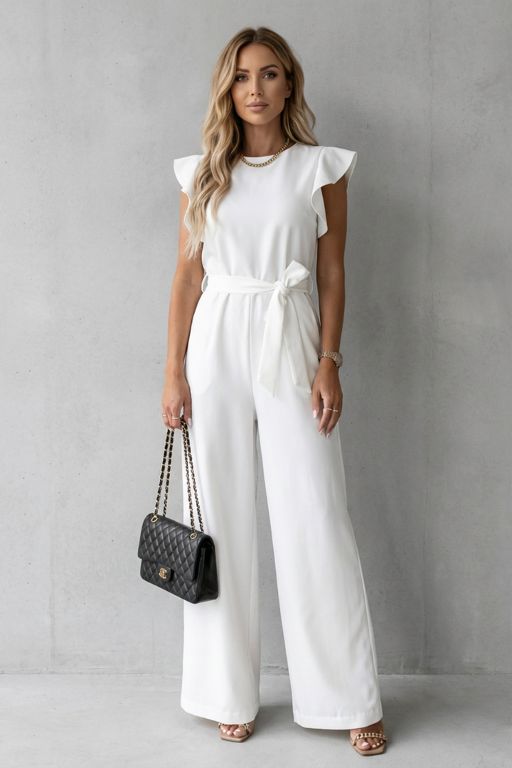 Front view of a woman wearing an elegant white ruffle sleeve belted wide-leg jumpsuit with a matching black handbag.