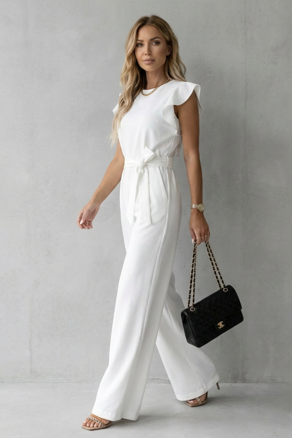 Side profile of a woman walking in the polished high-neck white jumpsuit with self-tie waist belt.