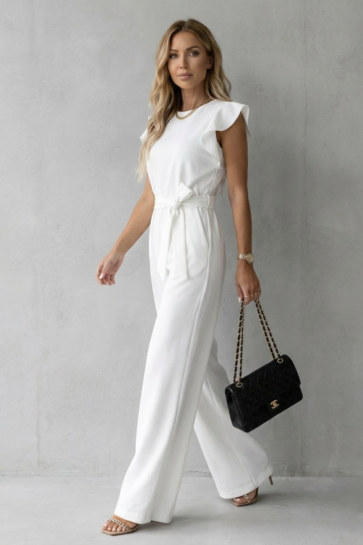 Side profile of a woman walking in the polished high-neck white jumpsuit with self-tie waist belt.