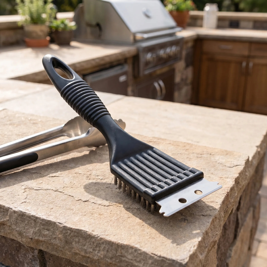 Black barbecue grill brush with textured handle placed near an outdoor grill station
