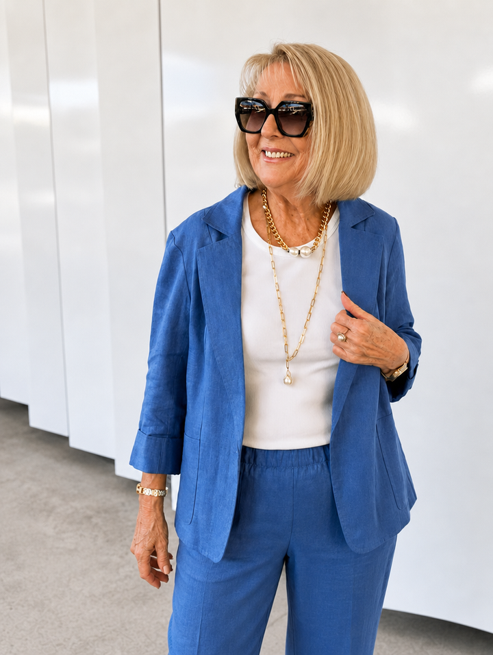 Older woman wearing a blue slim fit suiting set with a white top and gold necklace