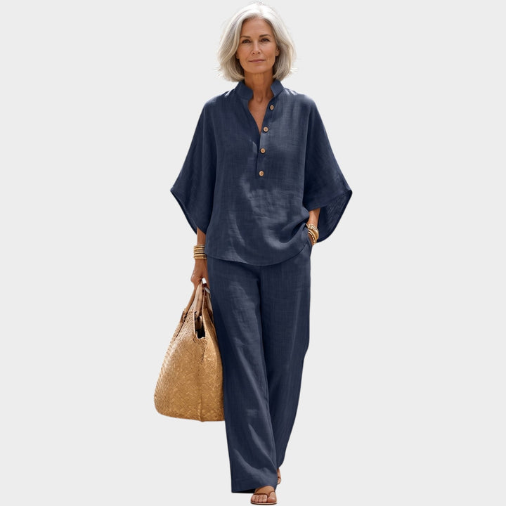 Older woman wearing a dark blue matching top and wide leg pants set holding a straw bag