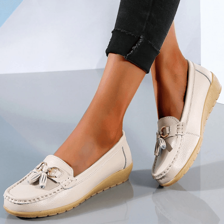Close-up of beige women's comfort loafer shoes with tassel detail worn with cropped black trousers.