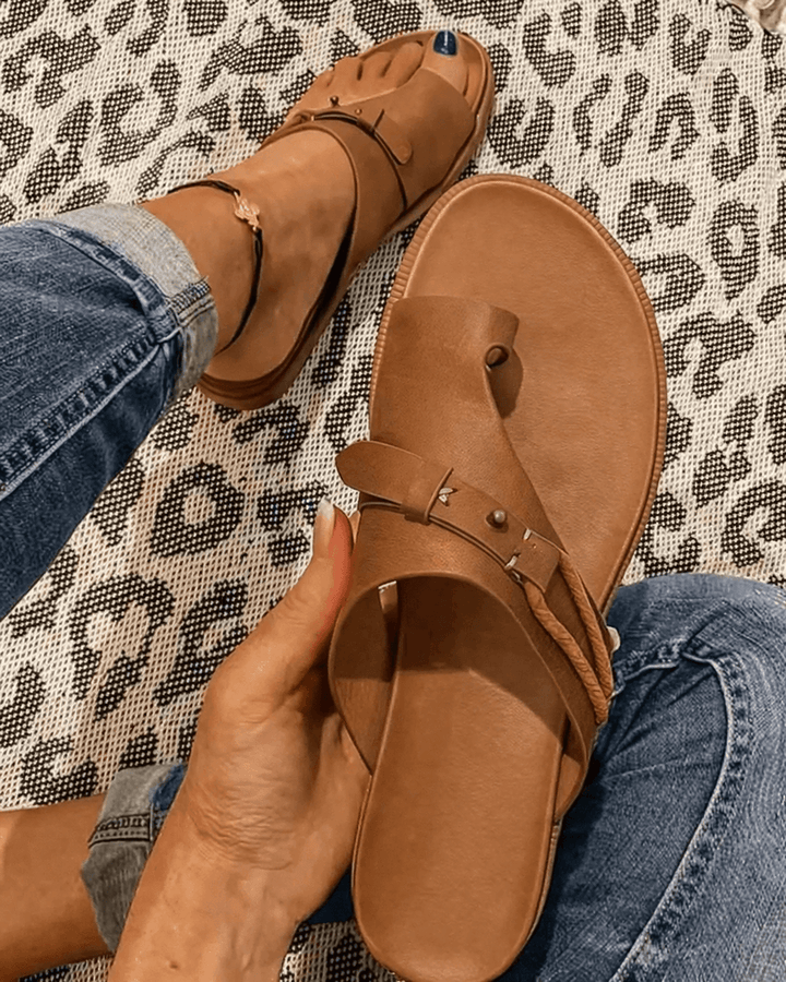 Women's brown toe-loop flat sandal held in hand against printed background