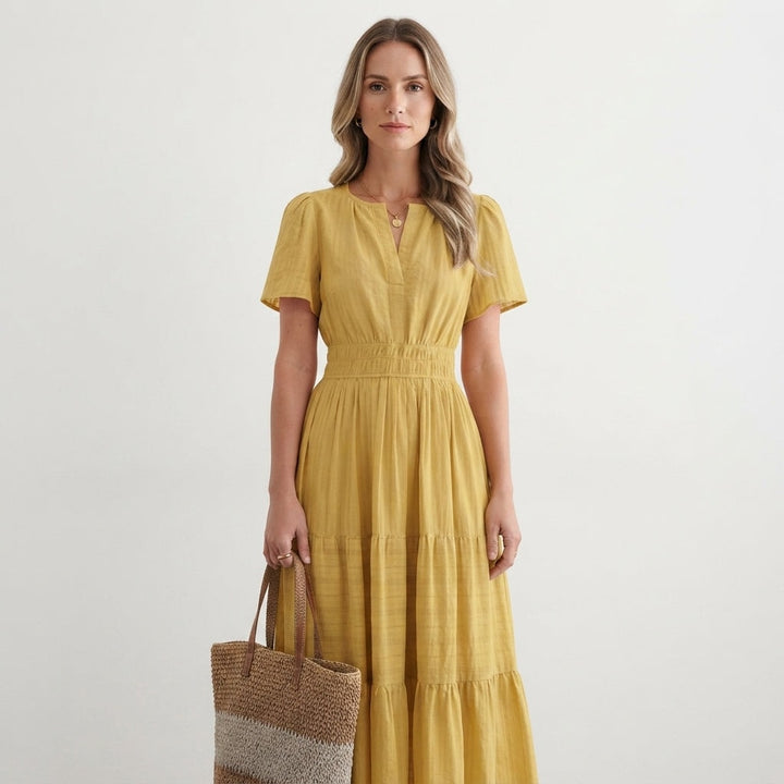 Model wearing a yellow tiered flutter-sleeve maxi dress holding a woven tote bag