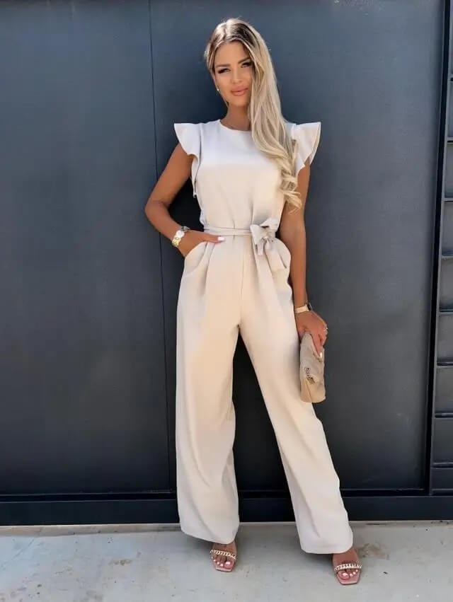 Front view of woman wearing a beige wide-leg jumpsuit with ruffle sleeves and belt