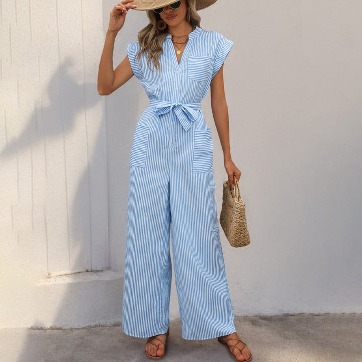 Front view of a woman wearing a blue and white striped wide-leg jumpsuit with a tie waist and straw hat.