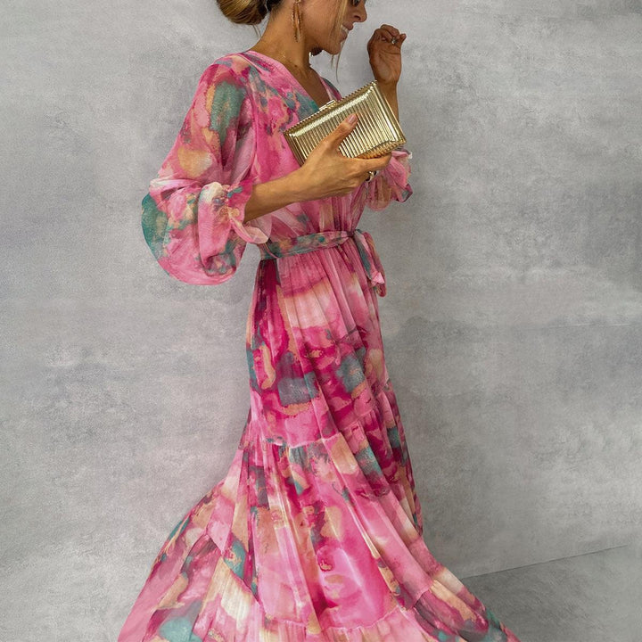 Model posing in a pink floral wrap maxi dress holding a gold clutch