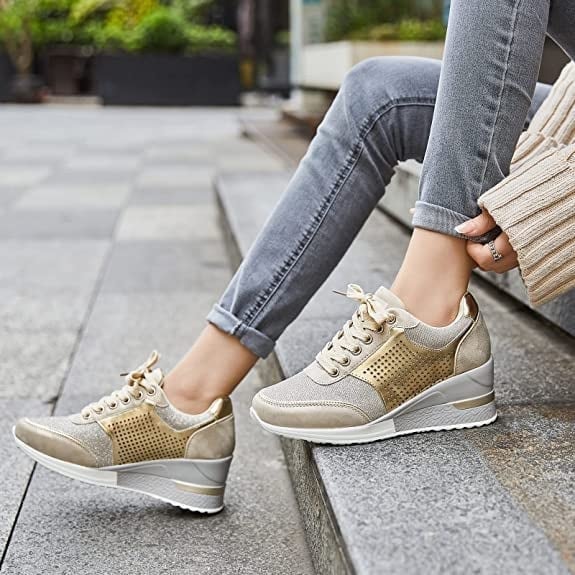 Woman wearing gold hidden wedge sneakers paired with grey jeans