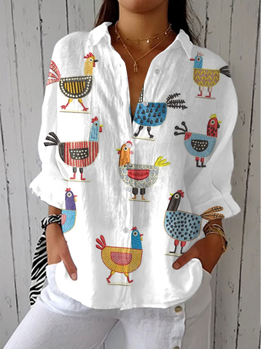 A woman wearing a white long-sleeve button-up blouse with a colorful chicken print and front pockets.