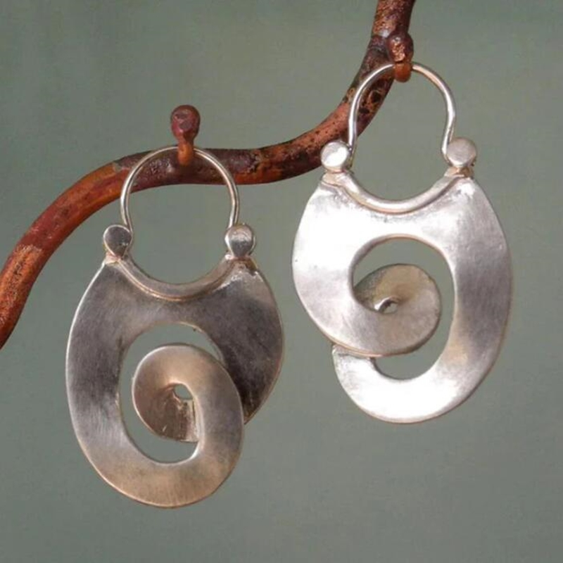 Women's vintage silver spiral statement earrings hanging on a decorative branch