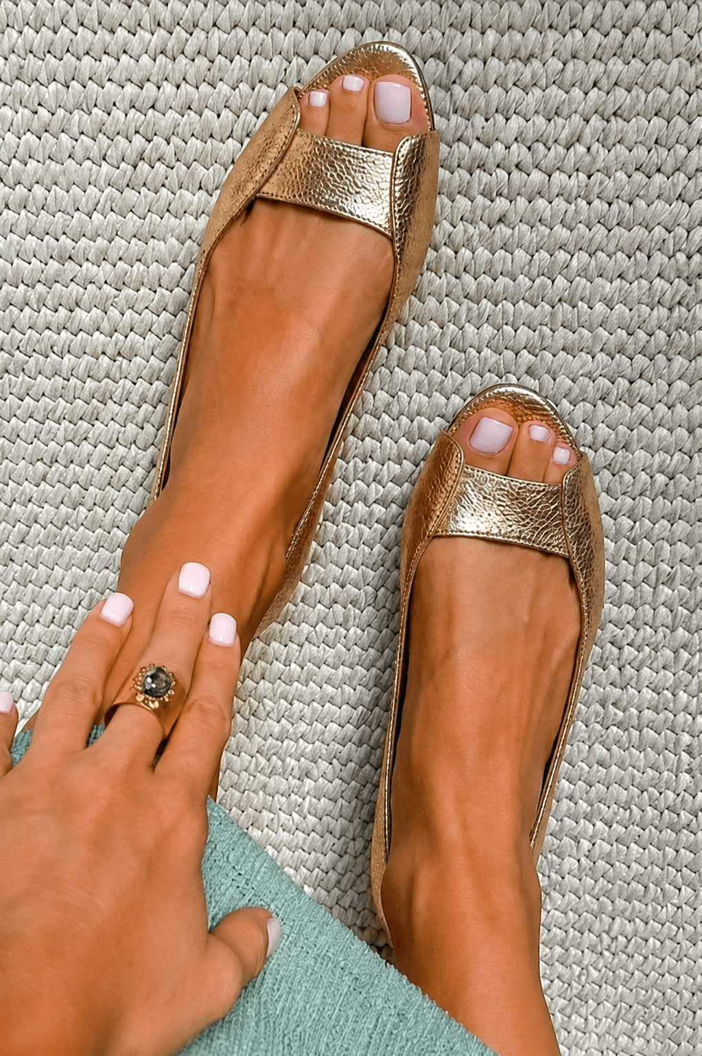Top view of gold metallic open-toe flat sandals paired with a textured light green garment.