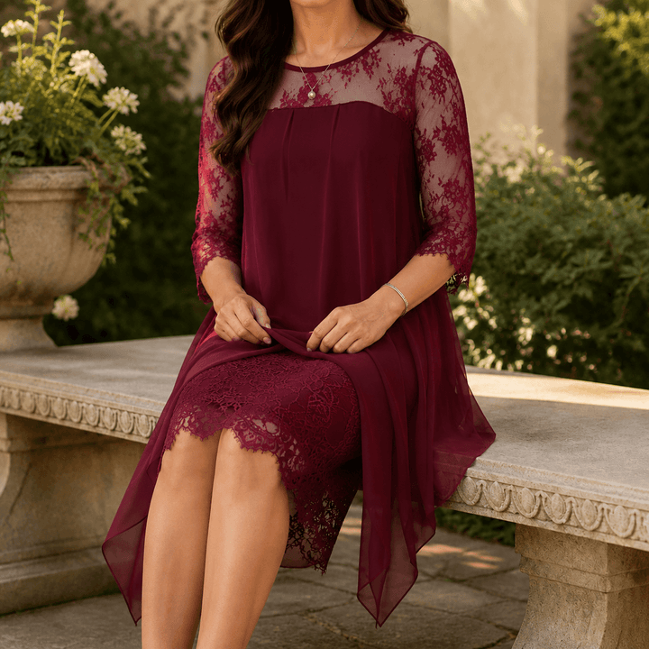 Close-up of a woman sitting on a stone bench wearing a burgundy midi dress with lace sleeves