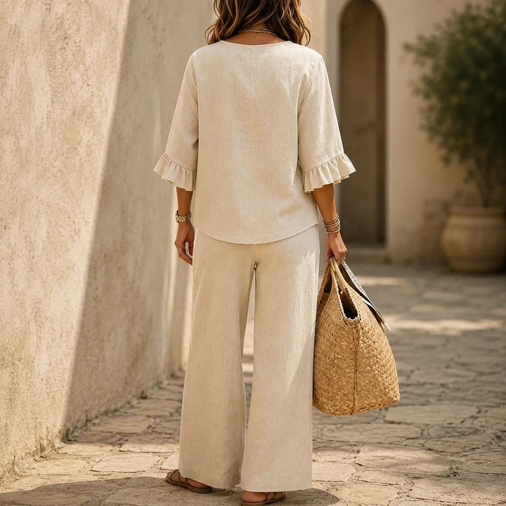 Back view of a woman wearing a beige two-piece outfit featuring a button top and matching wide-leg trousers