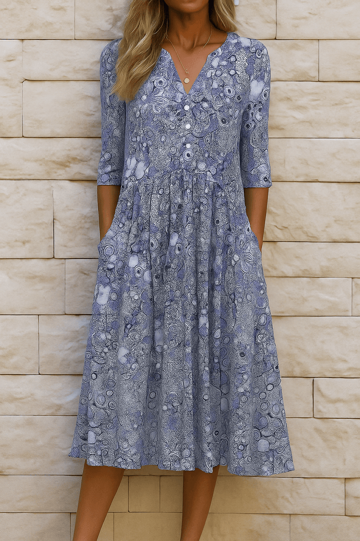 Woman wearing blue floral V-neck midi dress with pockets against a stone wall