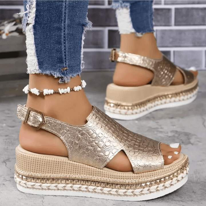 Close-up of gold platform wedge sandals featuring an adjustable ankle buckle and textured upper