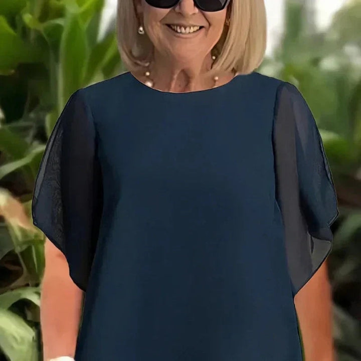 Detailed view of the sheer overlay neckline and short sleeves on the women's top