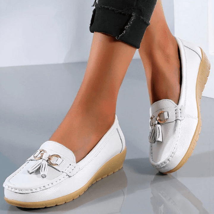 Detailed shot of white women's comfort loafer shoes featuring decorative metal buckle and tassel trim.