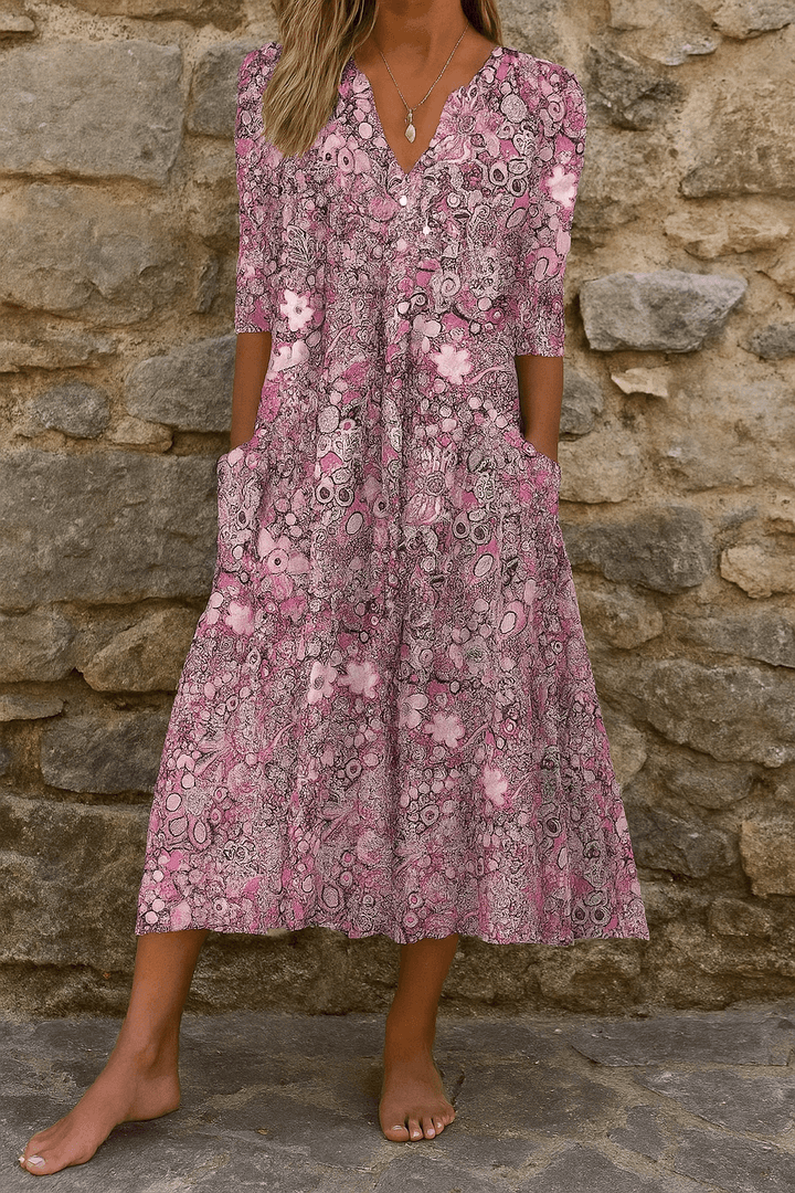 Woman wearing pink floral V-neck midi dress with pockets against a stone wall