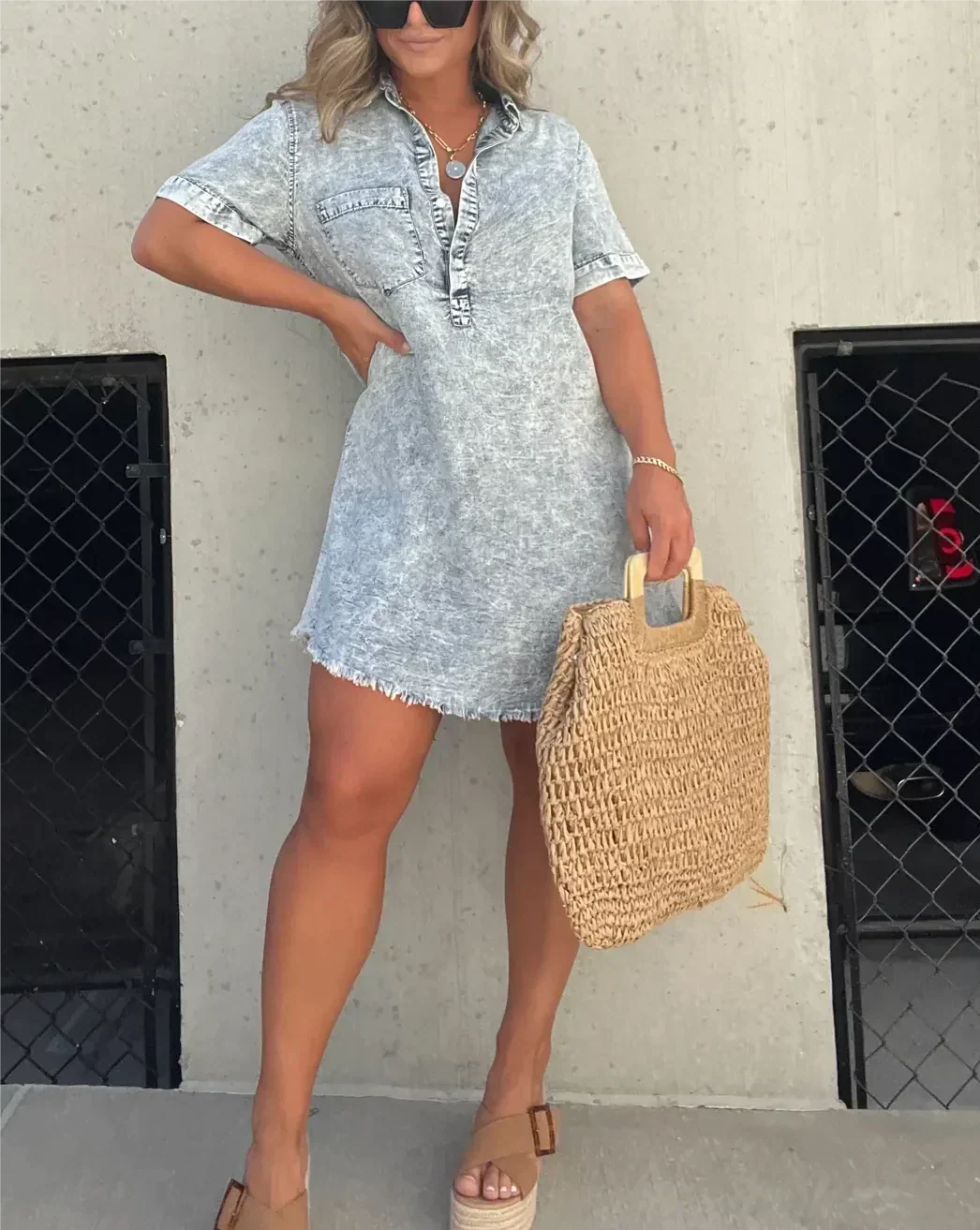 Woman wearing a stylish light wash denim shirt dress holding a straw bag