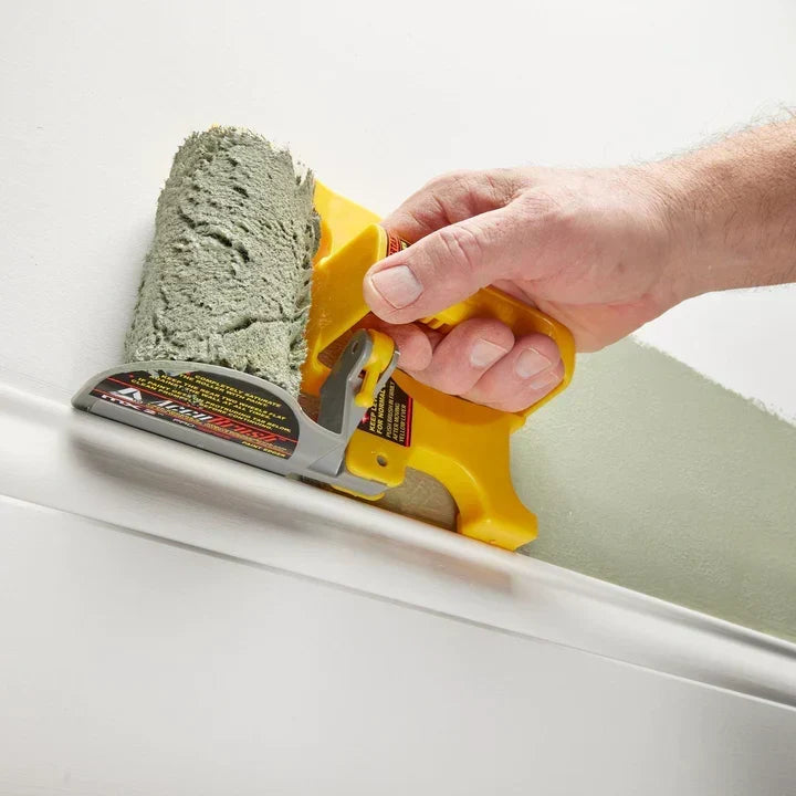 Hand using an edge paint roller along a baseboard with green paint