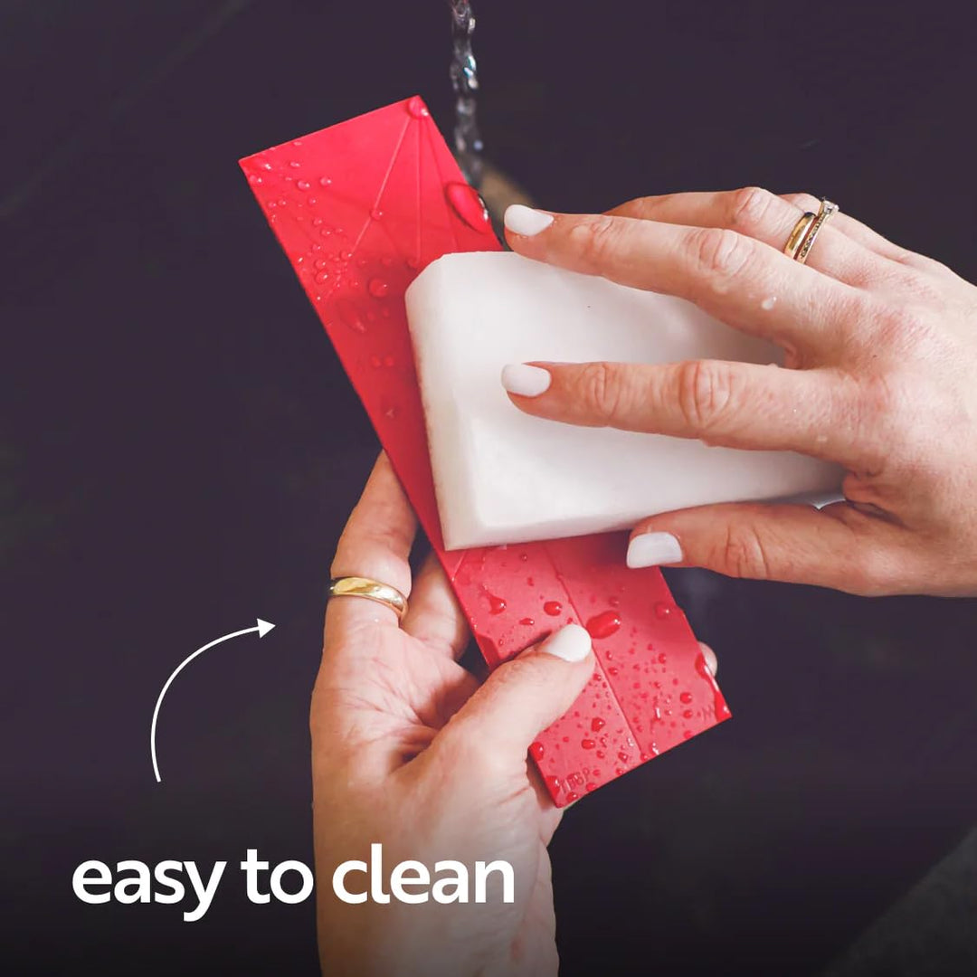 Hands washing a red silicone folding measuring spoon under running water with a sponge