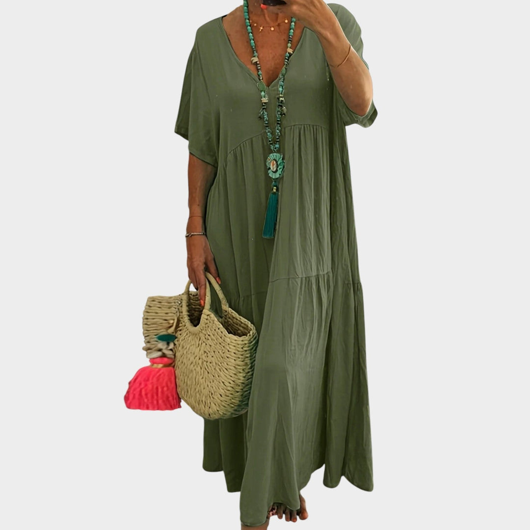 Woman wearing green plus size maxi dress with V-neck and tiered skirt holding woven bag