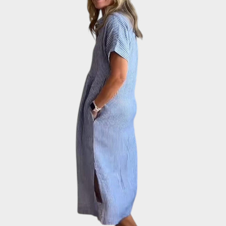 Side profile view of a woman wearing a blue striped maxi shirt dress with side slit