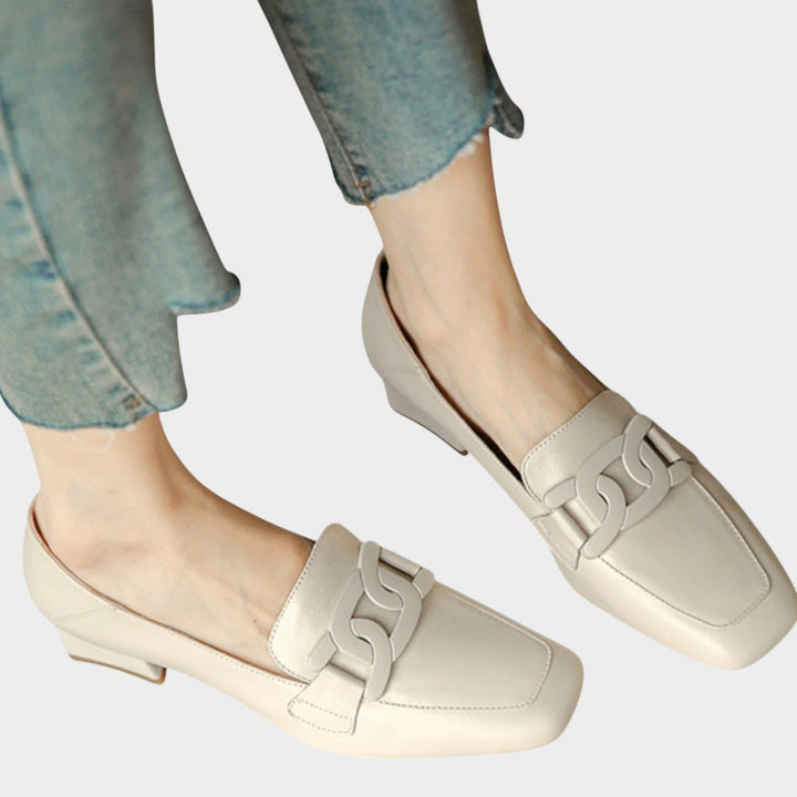 Woman wearing beige heeled loafers with decorative chain detail paired with jeans