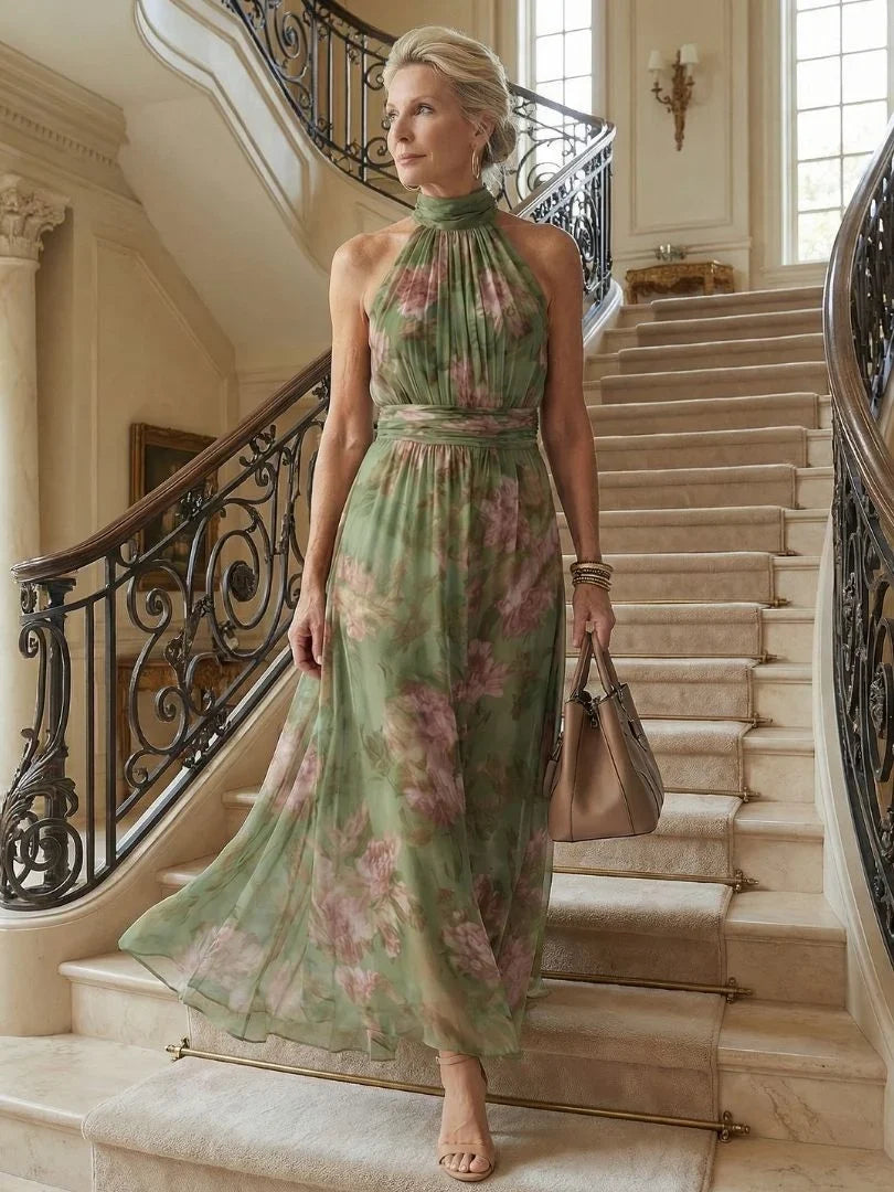 Woman descending a grand staircase wearing a green floral halter maxi dress.