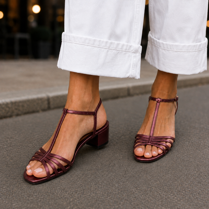 Close-up of women's rich burgundy metallic T-bar sandals styled with open-toe silhouette on a sidewalk