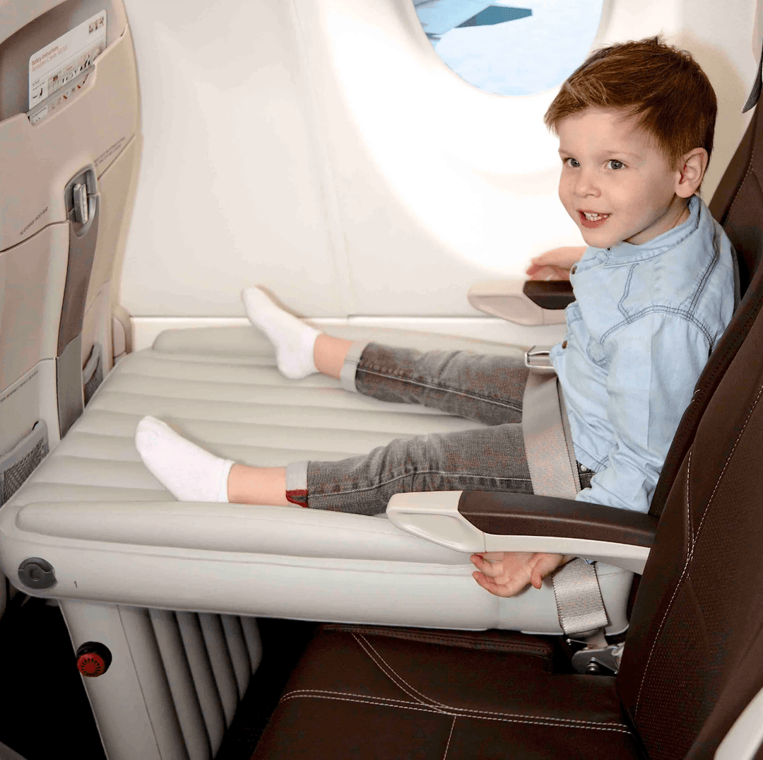 Young boy sitting comfortably on an inflatable airplane travel bed installed on an aircraft seat