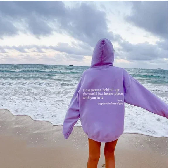 Back view of a woman wearing a light purple inspiring slogan casual hoodie on a beach