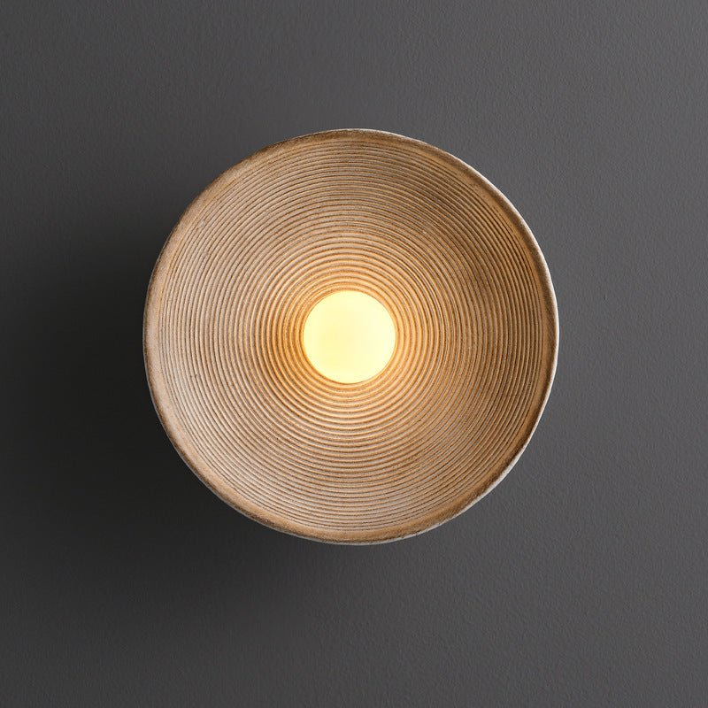 Close-up view of the circular wooden wall lamp lit up on a dark textured wall