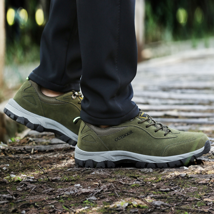 Green men's orthopedic hiking shoes worn outdoors on a wooden path