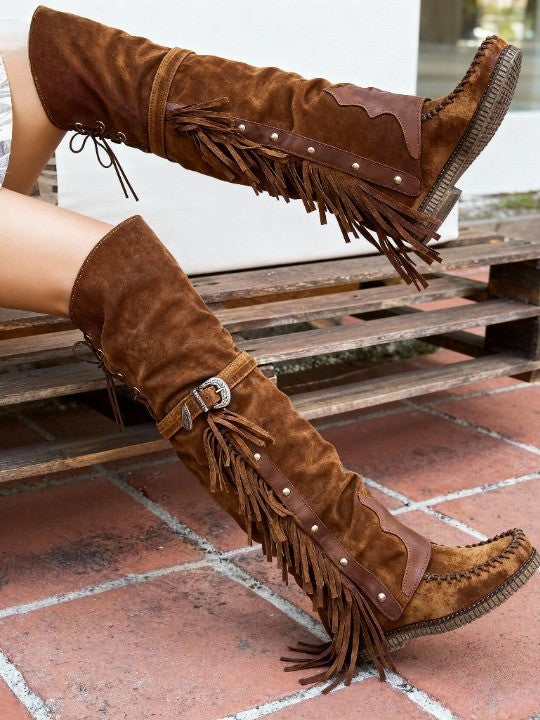 Brown over-the-knee tassel flat boots worn outdoors on a wooden bench