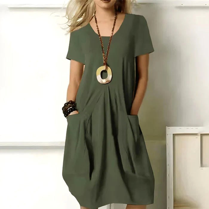 Woman wearing the green short sleeve relaxed dress with pockets and statement necklace