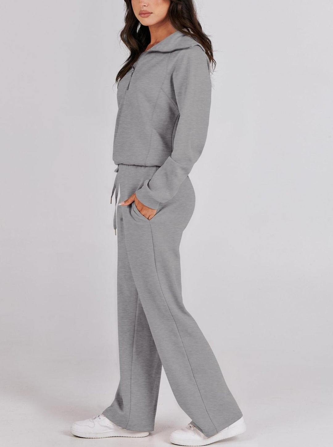 Side profile view of a woman wearing a grey half-zip loungewear set with straight-leg trousers and white sneakers.