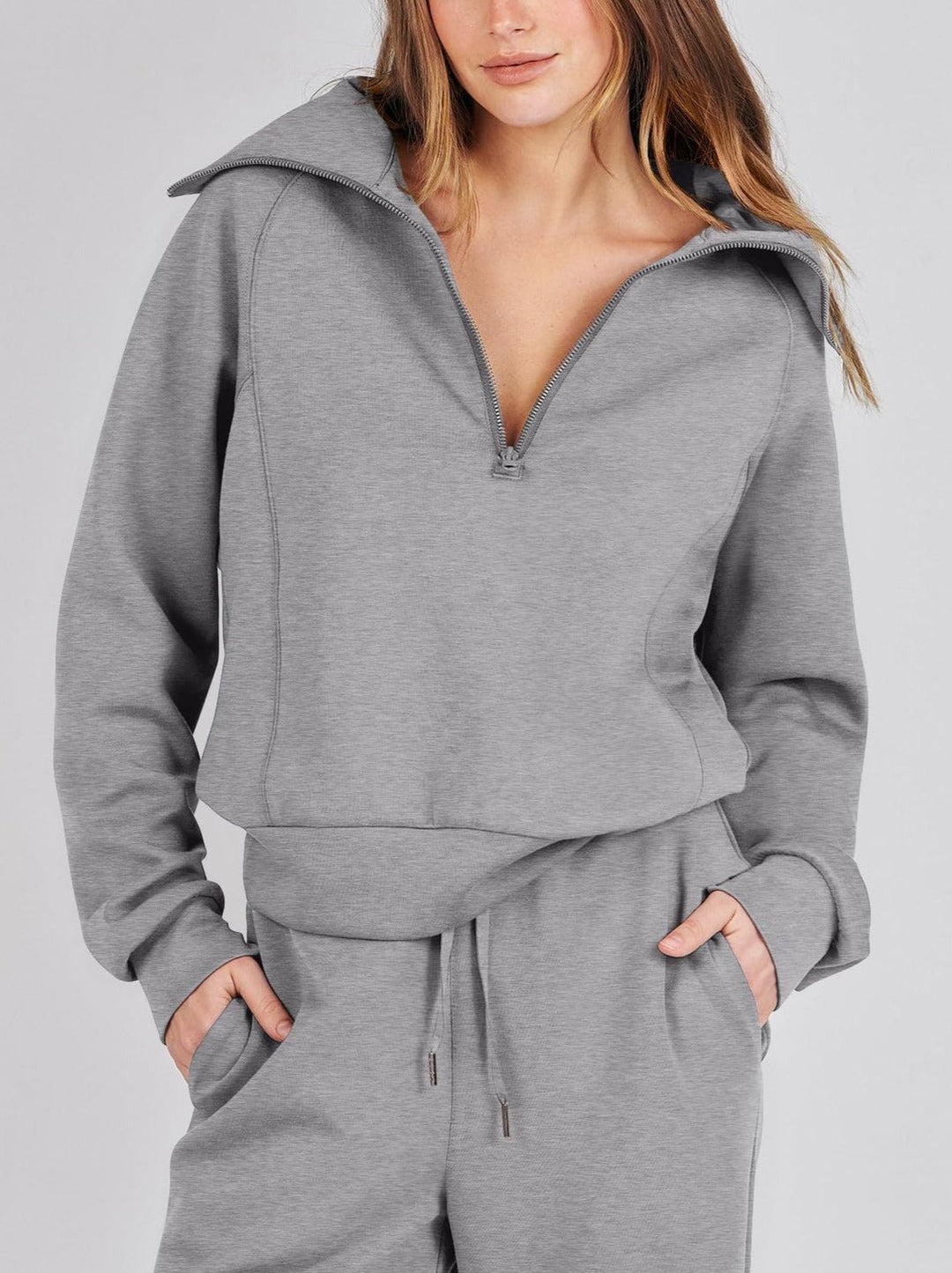 Close-up of a woman wearing the grey half-zip top featuring a stand-up collar and front pockets.