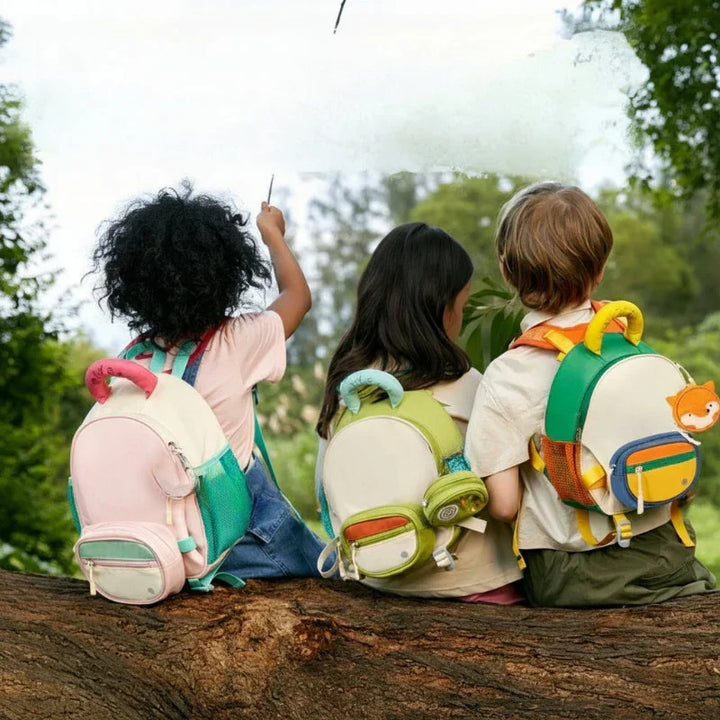 Children sitting outdoors wearing school backpacks in pink and green