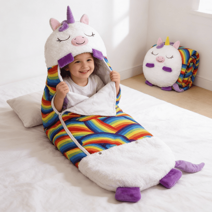 Happy child sitting inside a colorful white unicorn sleeping bag during daytime