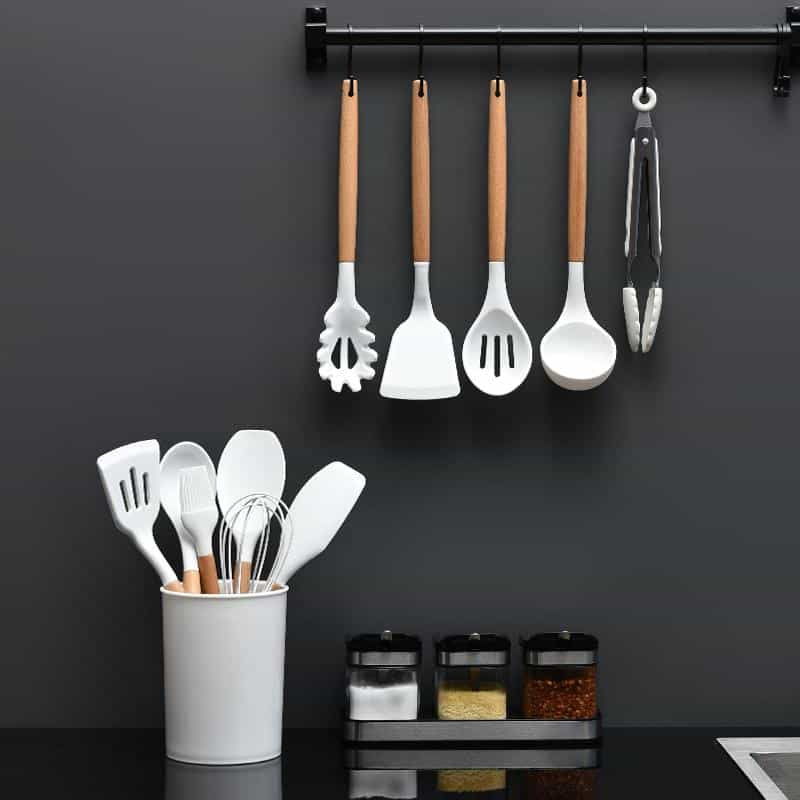 White silicone kitchen utensil set hanging and in holder against a dark wall