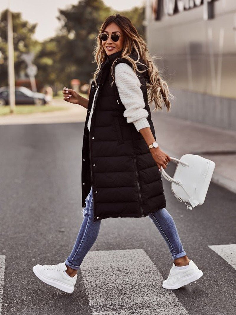 Walking profile view of woman wearing a black knee-length quilted bodywarmer and sneakers