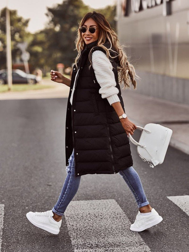 Walking profile view of woman wearing a black knee-length quilted bodywarmer and sneakers
