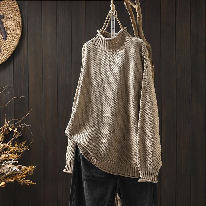 Beige women's cozy knitted pullover sweater hanging against a rustic wooden background